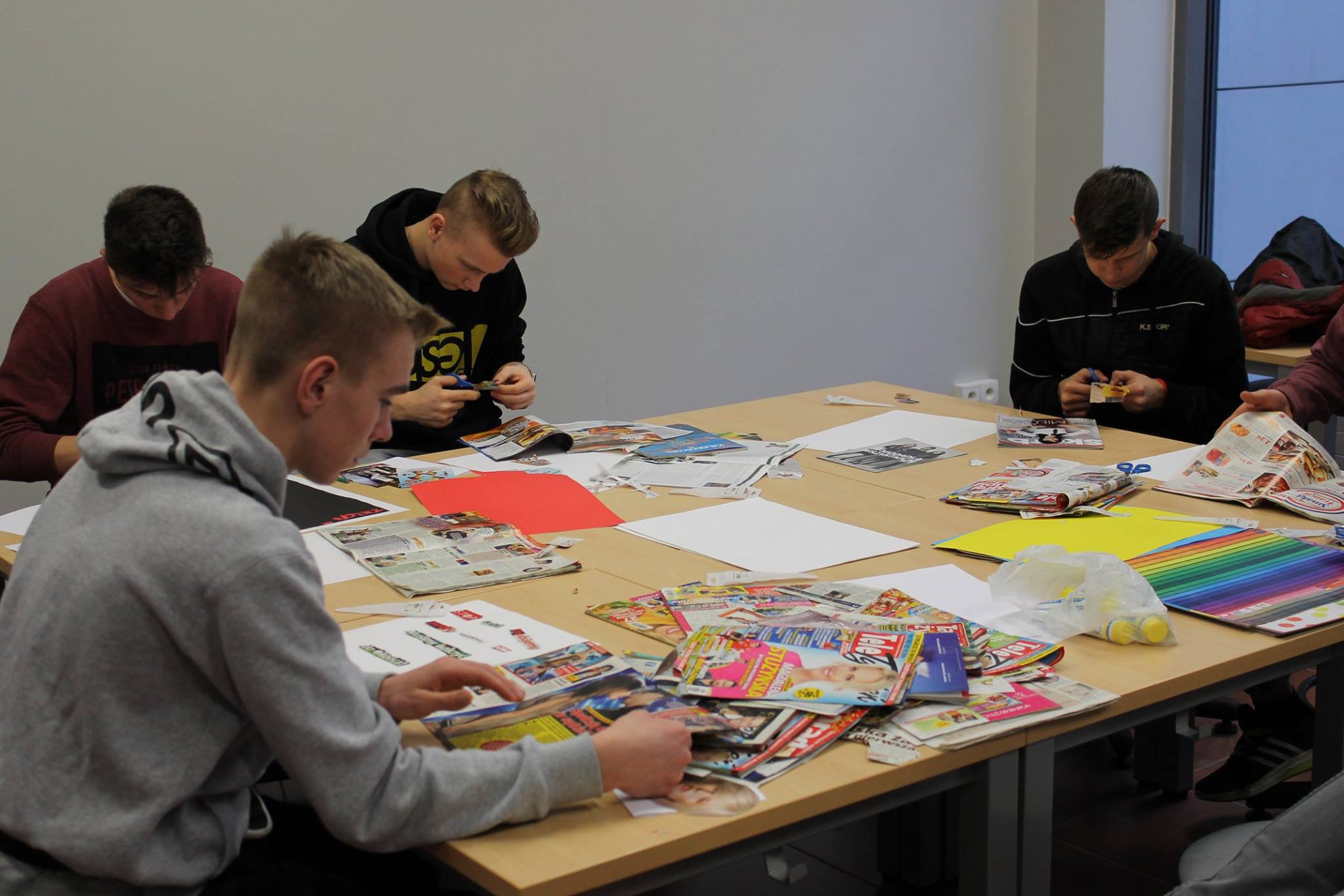 Studenci przy wielkim stole wycinają fragmenty z kolorowych pism 